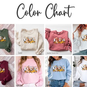 May include: Color chart featuring various colored sweatshirts. Each sweatshirt displays a Halloween-themed graphic with cartoon animals, pumpkins, and fall leaves. Colors include military green, sand, heather scarlet red, ash, maroon, light pink, light blue, and white.