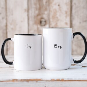May include: Two white ceramic mugs with black handles and black rims. The mug on the left is 11 oz and the mug on the right is 15 oz.