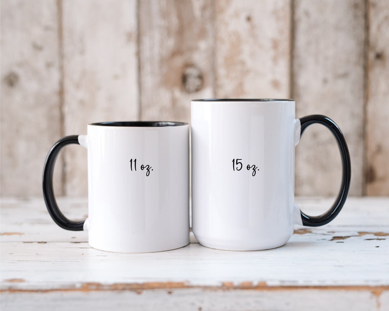 May include: Two white ceramic mugs with black handles and black rims. The mug on the left is 11 oz and the mug on the right is 15 oz.