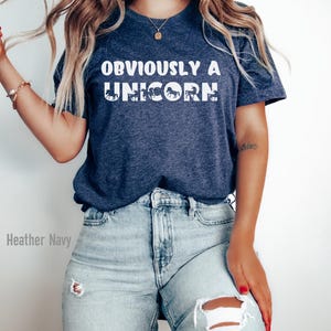 May include: A heather navy blue t-shirt with the text "OBVIOUSLY A UNICORN" in white. The text is made up of a series of unicorn silhouettes.