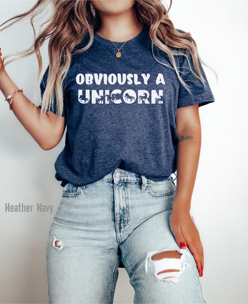 May include: A heather navy blue t-shirt with the text "OBVIOUSLY A UNICORN" in white. The text is made up of a series of unicorn silhouettes.