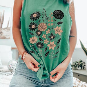 K&ouml;nnte beinhalten: Hellgr&uuml;nes Tanktop mit floralem Design. Die Grafik zeigt schwarze und pfirsichfarbene Blumen mit gr&uuml;nen Stielen und Bl&auml;ttern. Der Text "Light Green" ist in der unteren rechten Ecke sichtbar.