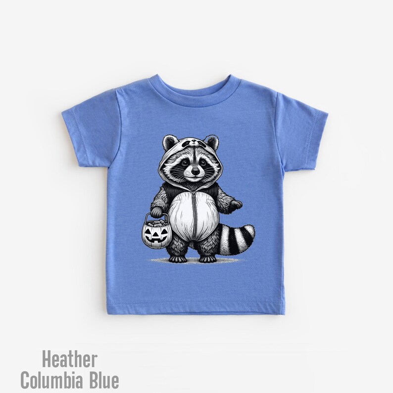 May include: A light blue t-shirt with a black and white illustration of a raccoon wearing a panda costume and holding a jack-o-lantern bucket. The raccoon is dressed for trick-or-treating.