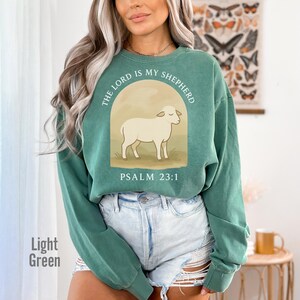 Op de afbeelding: Een lichtgroen sweatshirt met een witte schaap afbeelding en de tekst "The Lord is my Shepherd, Psalm 23:1".