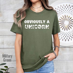 May include: A green t-shirt with the text "OBVIOUSLY A UNICORN" in white. The text is surrounded by a series of white unicorn silhouettes.