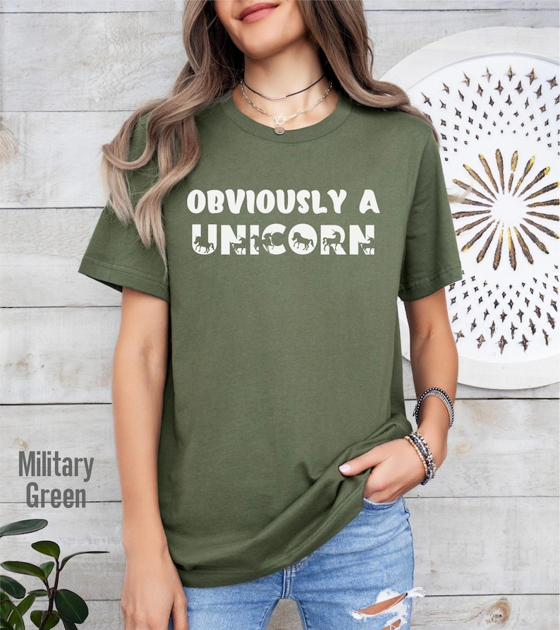 May include: A green t-shirt with the text "OBVIOUSLY A UNICORN" in white. The text is surrounded by a series of white unicorn silhouettes.