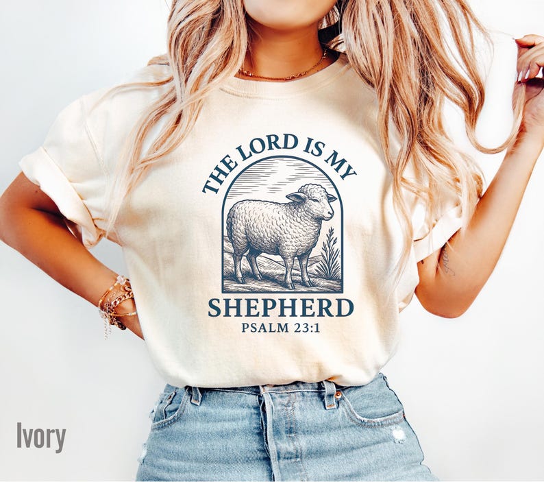 Puede incluir: Camiseta de color marfil con un gr&aacute;fico azul de una oveja y el texto "The Lord is my Shepherd Psalm 23:1"