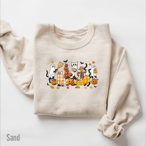 May include: Sand-colored sweatshirt featuring a Halloween-themed graphic. The graphic includes cartoon cats dressed as ghosts, pumpkins, and scarecrows. The word "Sand" is printed in the lower left corner.