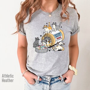May include: Gray t-shirt with a graphic of a pill bottle labeled "Serotonin Booster" with cute cartoon cats spilling out of it.