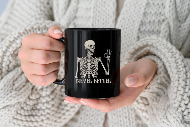 Op de afbeelding: Zwarte koffiemok met een witte skelet afbeelding en de tekst "Never Better".