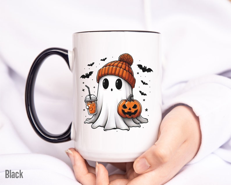 May include: White ceramic mug with a black rim and handle. The mug features a cartoon ghost wearing an orange and brown knit hat, holding a pumpkin and a cup of orange juice. The background is white with black bats and stars.
