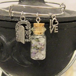 May include: A silver charm bracelet with three charms: a small glass bottle filled with dried lavender and white crystals, a charm with the words "I LOVE" and a heart, and a charm with the words "GARDEN" and a gate.