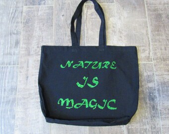 May include: Black canvas tote bag with green glitter lettering that reads "Nature is Magic".