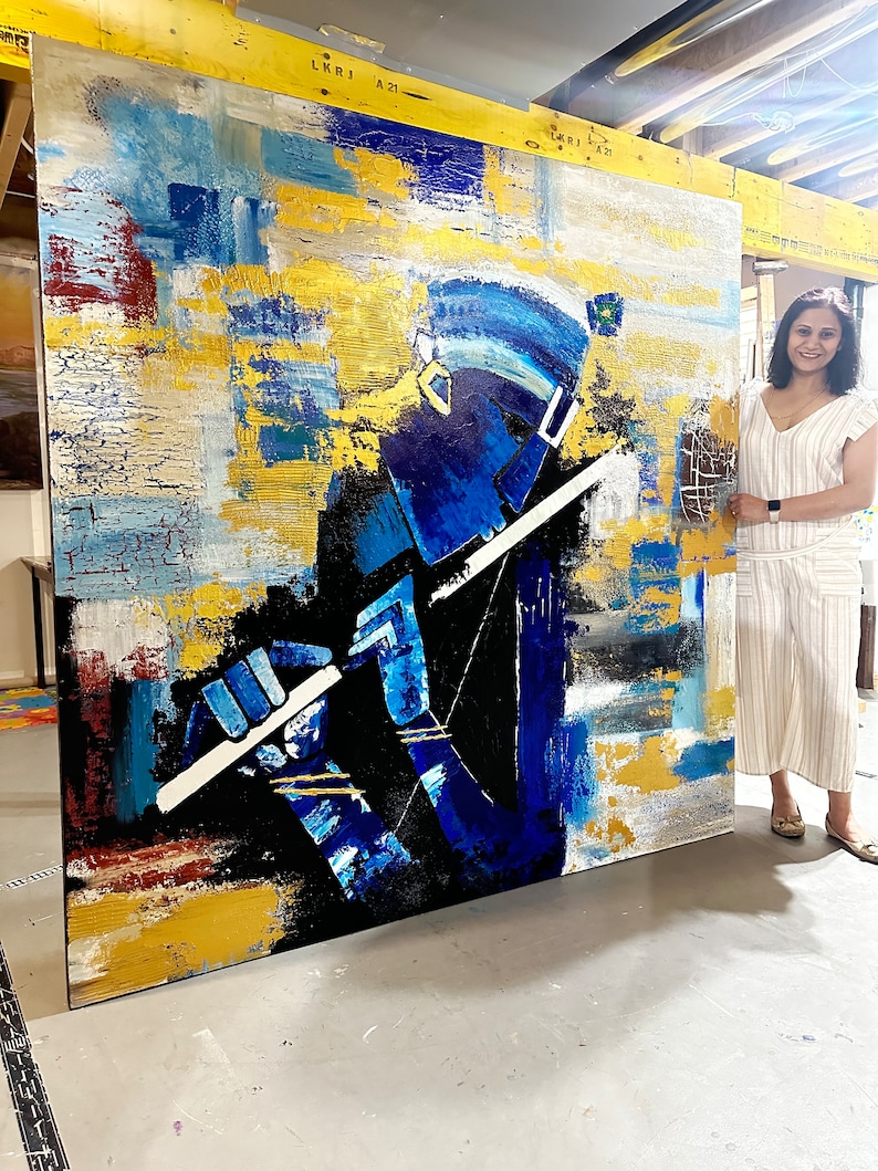 May include: Abstract painting of a person playing a flute, with a blue, gold, and white colour scheme. The painting is large and is leaning against a wall.