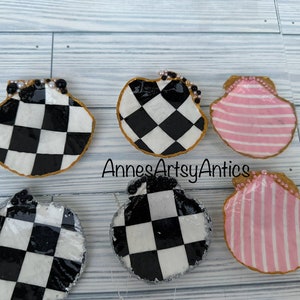 May include: Five decorative seashell trinket dishes. Two are black and white checkered, two are pink and white striped, and one is gray and white checkered. Each dish has a gold rim and pearl accents.