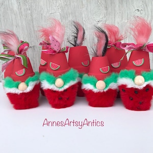 May include: Five watermelon gnome decorations. Each gnome is made from a terracotta pot painted red with a watermelon slice design. The gnomes have white and green fur trim, red fur bodies, and pink and black hair.