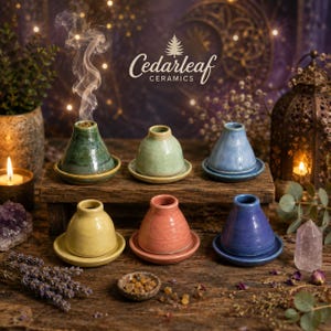 May include: Six ceramic incense burners in various colors including green, light green, blue, yellow, pink, and dark blue. Each burner consists of a conical top piece with a central hole and a matching circular base plate, arranged on a wooden stand.