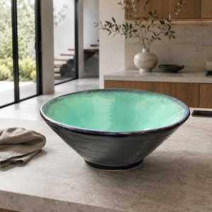 May include: A large, wide-rimmed bowl featuring a smooth, glossy mint green interior that transitions into a dark, textured charcoal gray exterior. The bowl has a rounded, tapered base and a slightly uneven, organic rim with a dark finish.