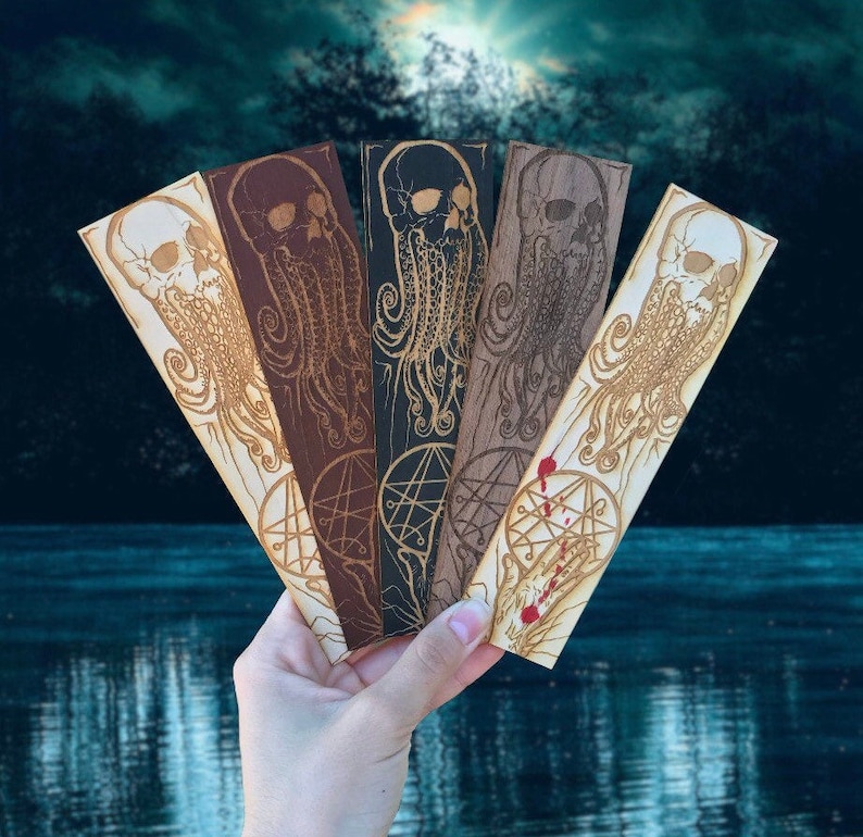 May include: Set of five wooden bookmarks featuring a skull with tentacles design. Each bookmark has a different color and features a pentagram symbol.