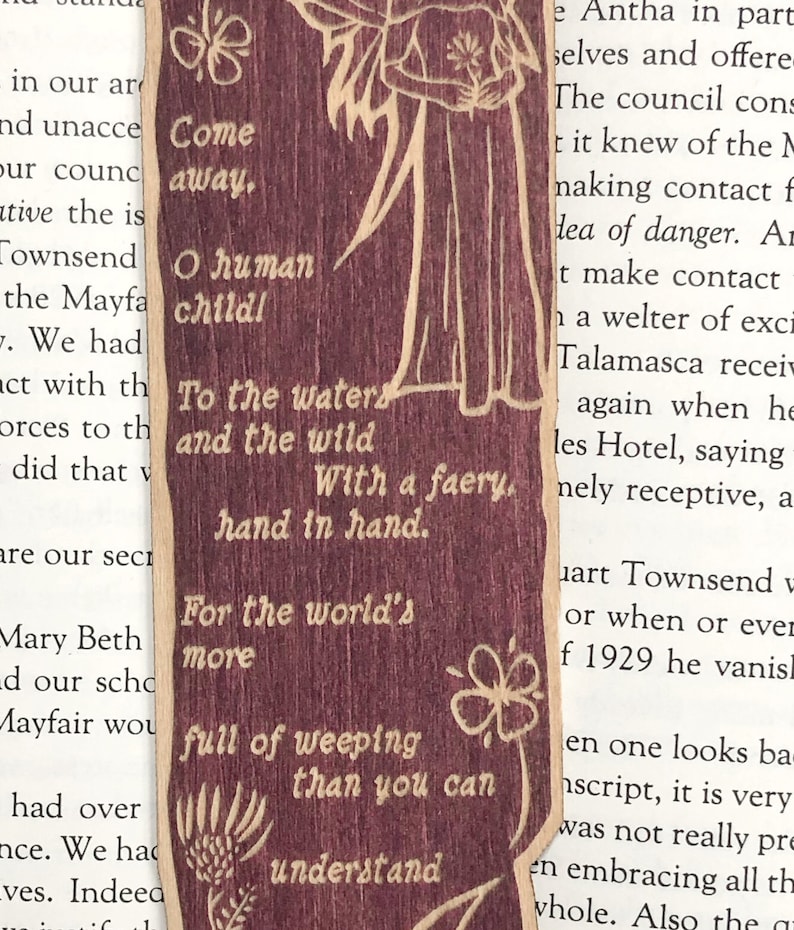 May include: A wooden bookmark with a whimsical illustration of a fairy with wings and a flower. The bookmark features the text "Come away, O human child! To the waters and the wild With a faery, hand in hand. For the world's more full of weeping than you can understand."
