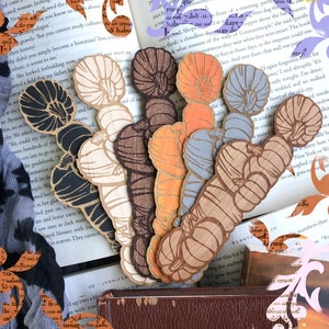 May include: A set of six wooden bookmarks featuring a carved pumpkin design. The bookmarks are painted in various colors, including black, white, brown, orange, and blue.