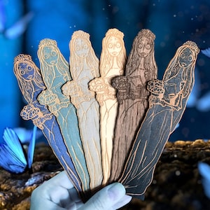Puede incluir: Conjunto de seis marcapáginas de madera con un diseño caprichoso de mujeres con cabello largo y fluido y detalles intrincados. Los marcapáginas están pintados en tonos de gris, marrón y negro.