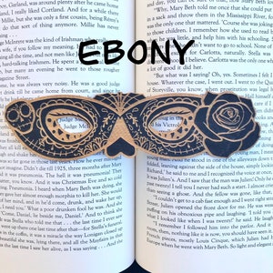May include: A pair of wooden masquerade masks with intricate black and white designs. The masks are shaped like butterflies and have a cutout in the center of each eye. The text "Judge Me" is visible on one mask.