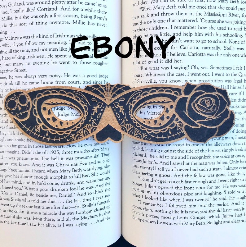 May include: A pair of wooden masquerade masks with intricate black and white designs. The masks are shaped like butterflies and have a cutout in the center of each eye. The text "Judge Me" is visible on one mask.