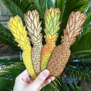 Può includere: Quattro ornamenti in legno a forma di ananas in diverse tonalità di giallo, verde e marrone. Gli ornamenti sono dipinti a mano e presentano un design dettagliato.