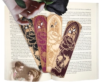May include: Four wooden bookmarks with laser-cut designs. The bookmarks feature a gothic archway, a rose, and a skull. The bookmarks are in shades of black, purple, and brown.