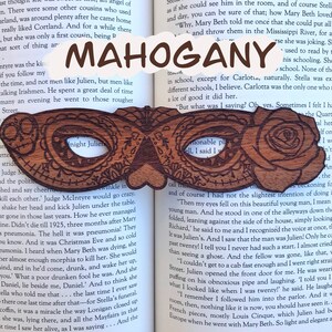 May include: A wooden bookmark shaped like a masquerade mask with intricate carvings. The bookmark is made of mahogany wood and features the text "Night Julien" on the left side and "Mahogany" on the right side.