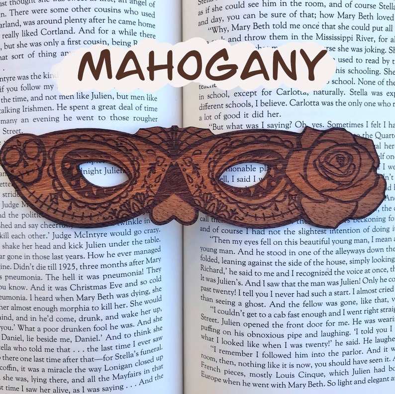 May include: A wooden bookmark shaped like a masquerade mask with intricate carvings. The bookmark is made of mahogany wood and features the text "Night Julien" on the left side and "Mahogany" on the right side.