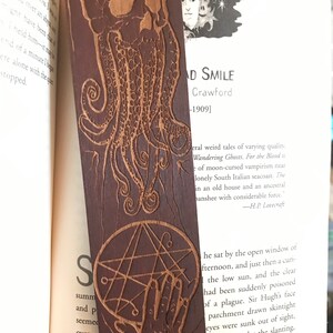 May include: A wooden bookmark with a dark brown finish. The bookmark features a detailed carving of a skull with tentacles and a pentagram. The text "AD SMILE Crawford -1909]" is visible on the bookmark.