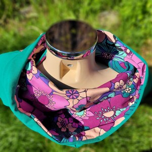 May include: A teal cowl neck scarf with a pink and purple floral print. The scarf is reversible and can be worn with either side showing.