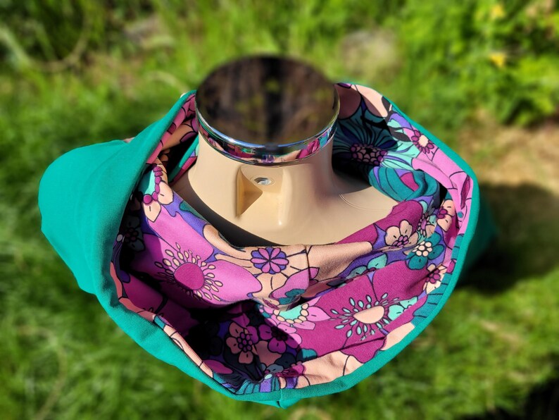 May include: A teal cowl neck scarf with a pink and purple floral print. The scarf is reversible and can be worn with either side showing.