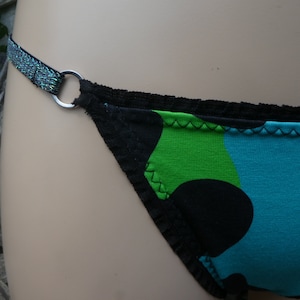 Könnte beinhalten: Schwarze und grüne Unterwäsche mit schwarzem Besatz und einem silbernen Ring. Die Unterwäsche hat ein blaues und grünes Punkte-Muster.