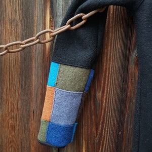 May include: Black fleece jacket with a colourful patchwork sleeve. The sleeve is made of different coloured fabrics, including blue, green, orange, and grey.