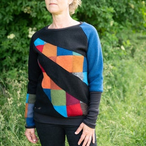 May include: A black sweater with a colourful patchwork design on the front. The sweater has blue sleeves and a black collar.