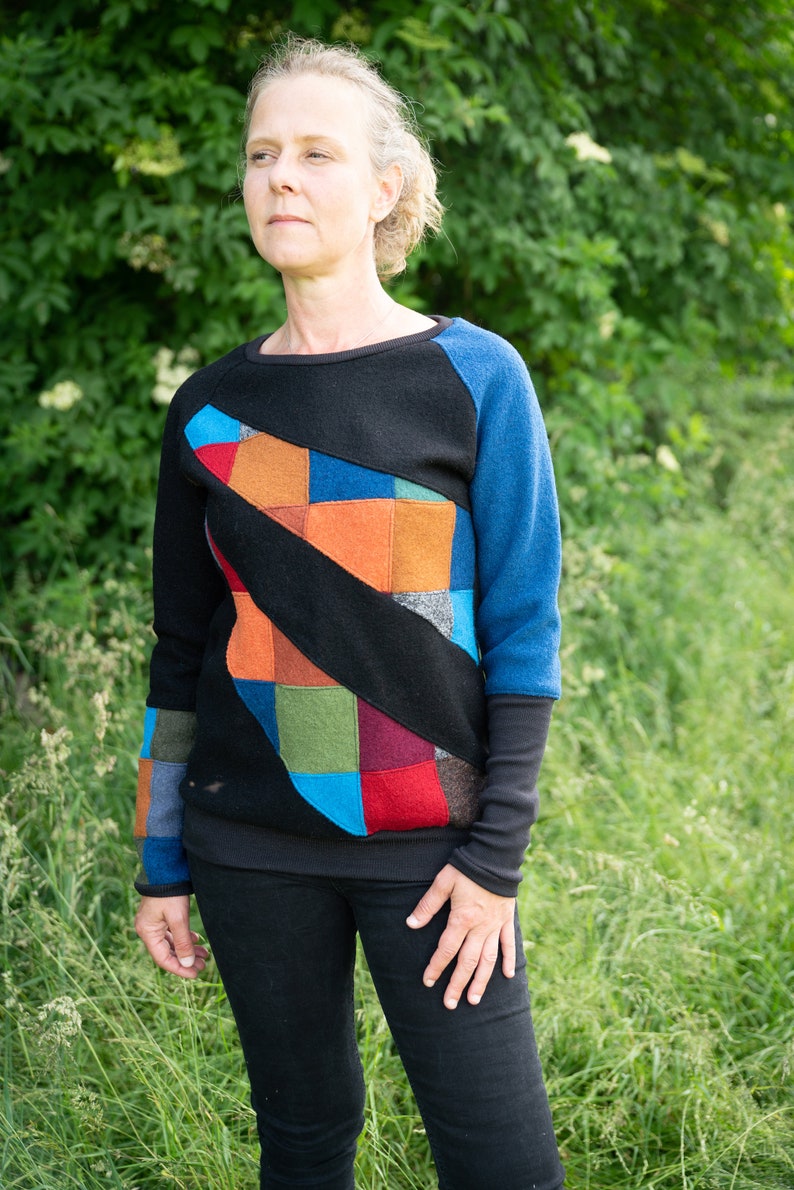 May include: A black sweater with a colourful patchwork design on the front. The sweater has blue sleeves and a black collar.