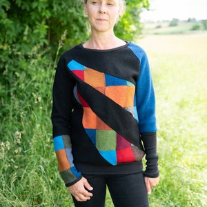 May include: A black sweater with a colourful patchwork design on the front. The sweater has long sleeves and a crew neck.