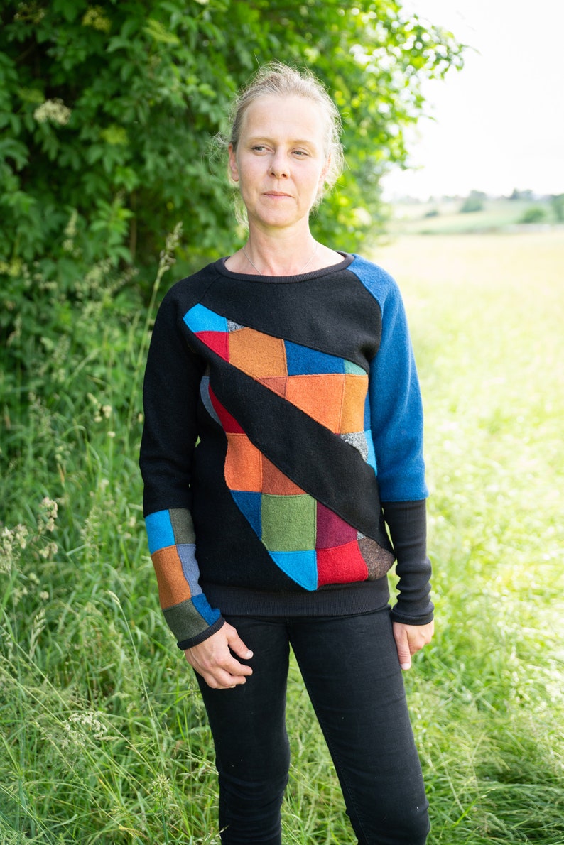 May include: A black sweater with a colourful patchwork design on the front. The sweater has long sleeves and a crew neck.