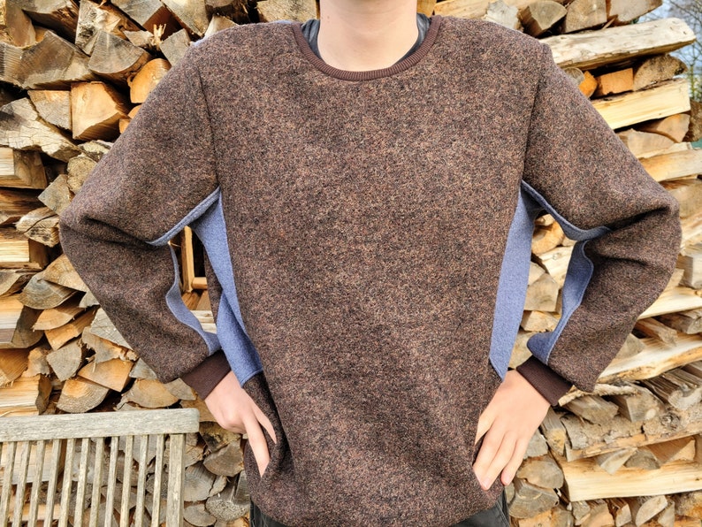 Pode incluir: Um su&eacute;ter marrom com pain&eacute;is de tecido azul nas mangas. O su&eacute;ter tem gola redonda e um tric&ocirc; texturizado.