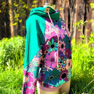 May include: A turquoise and pink hooded sweatshirt with a floral print. The sweatshirt has a drawstring hood and a contrasting color panel on the sleeves.