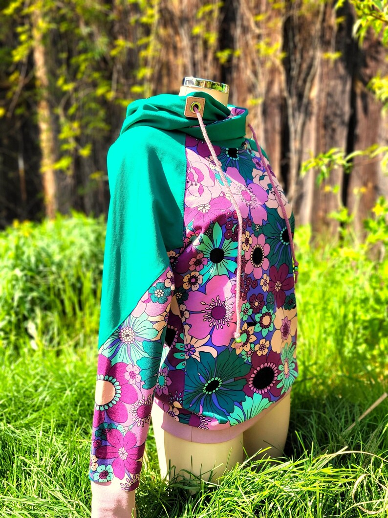 May include: A turquoise and pink hooded sweatshirt with a floral print. The sweatshirt has a drawstring hood and a contrasting color panel on the sleeves.