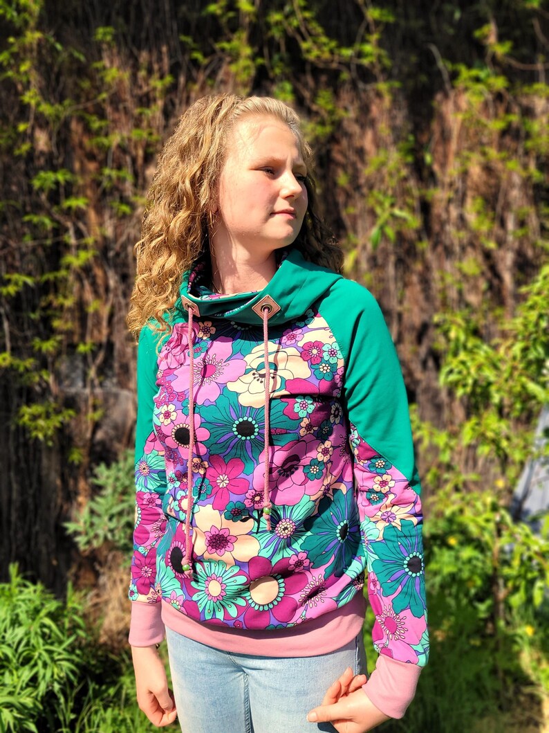 May include: A teal and pink hooded sweatshirt with a floral print. The hoodie has a cowl neck and a drawstring.