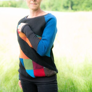 May include: A black sweater with a colourful patchwork design on the front and blue sleeves. The sweater has a relaxed fit and a round neckline.
