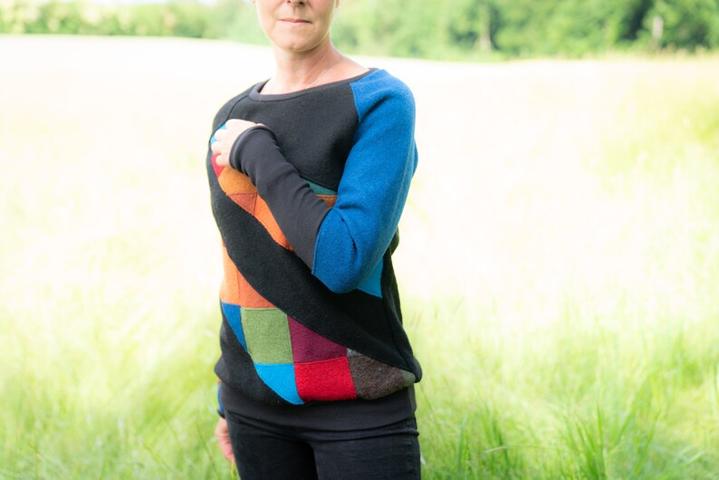 May include: A black sweater with a colourful patchwork design on the front and blue sleeves. The sweater has a relaxed fit and a round neckline.