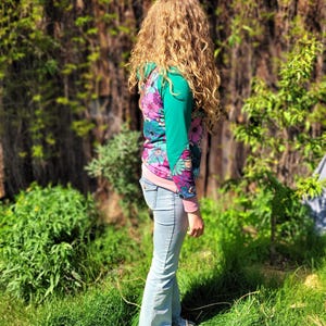 May include: A woman wearing a pink, green, and blue floral print long-sleeved shirt with a light blue pair of jeans.