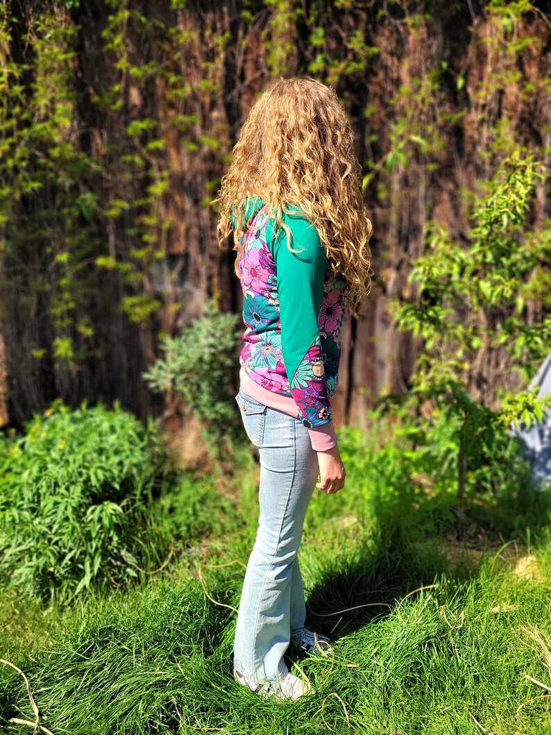 May include: A woman wearing a pink, green, and blue floral print long-sleeved shirt with a light blue pair of jeans.