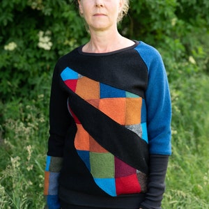 May include: A black sweater with a colourful patchwork design on the front. The sweater has long sleeves and a crew neck.